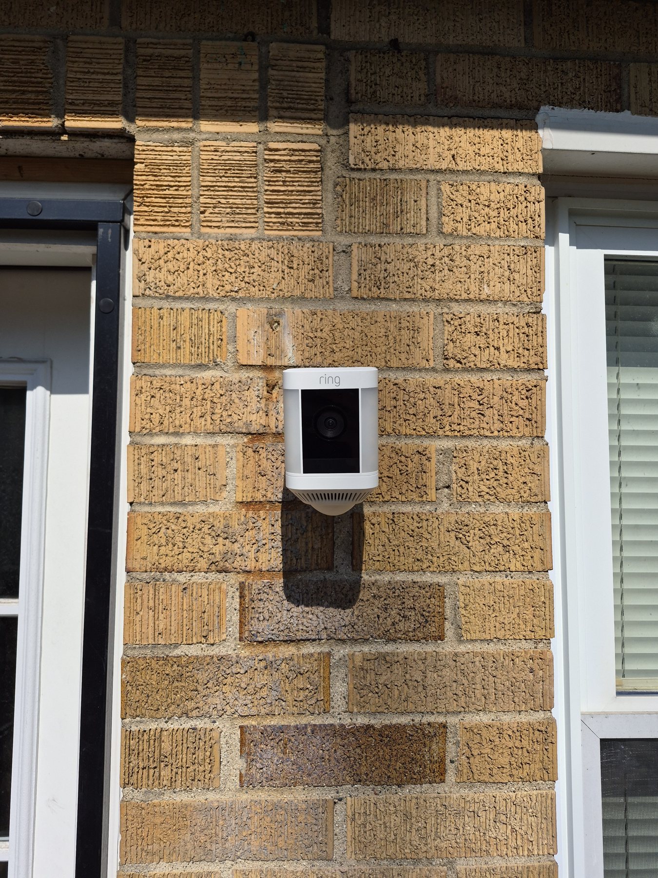 Ring security camera mounted on brick between a residential door and window
